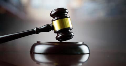 "Photo d'un marteau de juge en bois avec une tête dorée, posé sur un socle en bois. L'image évoque le thème de la justice."