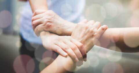 "Photo montrant des mains entrelacées, symbolisant le soutien, la solidarité ou la connexion humaine, avec un flou artistique coloré en arrière-plan."