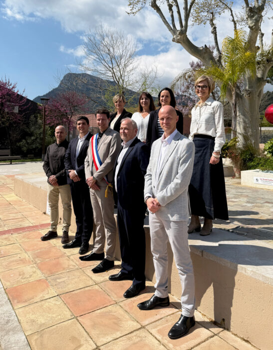 Le maire portant une écharpe tricolore pose avec ses adjoints sur une place extérieure.