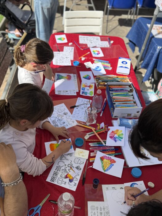 Atelier créatif lors du Printemps du Coudon, où des enfants et des adultes sont assis autour d’une table recouverte de feuilles à colorier, de feutres, de crayons, et de peintures. Les participant·e·s, concentré·e·s, laissent libre cours à leur imagination sur des dessins variés. L’ambiance est conviviale et intergénérationnelle.