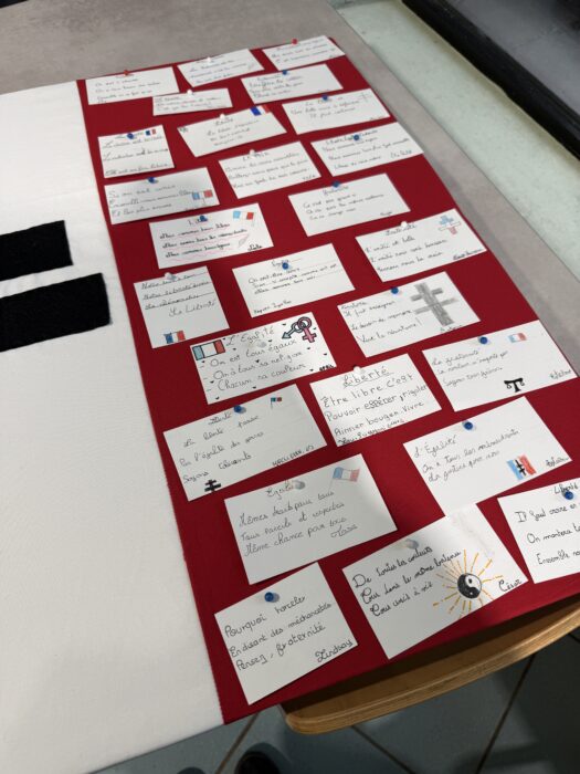 Panneau d’expression réalisé par les élèves du collège André-Malraux de La Farlède lors de la cérémonie de transmission du drapeau Unadif. Des cartes et des post-it sont accrochés sur un fond rouge, avec des messages manuscrits sur les valeurs de liberté, d’égalité, de fraternité, de résistance et de paix. Certains messages sont illustrés de dessins symboliques comme des drapeaux, des croix ou des soleils.