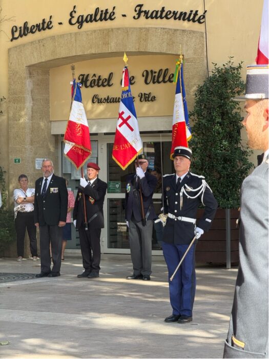 Prise de commandement de la brigade de gendarmerie de La Farlède par le lieutenant Jaillet. Des militaires au garde-à-vous, avec drapeaux et épées, devant la mairie surmontée de la devise 'Liberté - Égalité - Fraternité'.