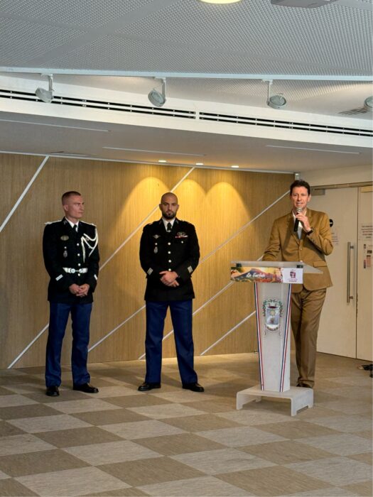Prise de commandement de la brigade de gendarmerie de La Farlède. Le maire Yves Palmieri prononce un discours au pupitre, tandis que le lieutenant Jaillet et un autre militaire, en uniforme, écoutent debout.