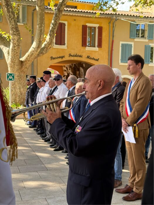 Prise de commandement de la brigade de gendarmerie de La Farlède. Un trompettiste en costume noir joue devant un groupe d'officiels en uniforme et en costume, dont le maire Yves Palmieri en écharpe tricolore, devant un bâtiment beige.